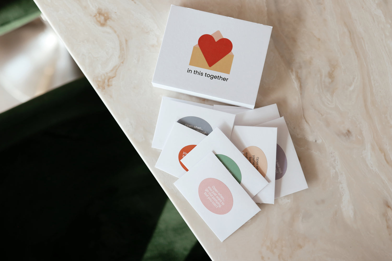 A box of in this together cards, with the 12 cards spread out on a marble worktop. 