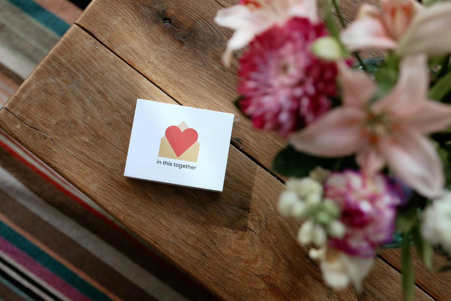 A box of 12 in this together cards - the perfect gift for any new Mum. On a wooden table next to some pink flowers. 