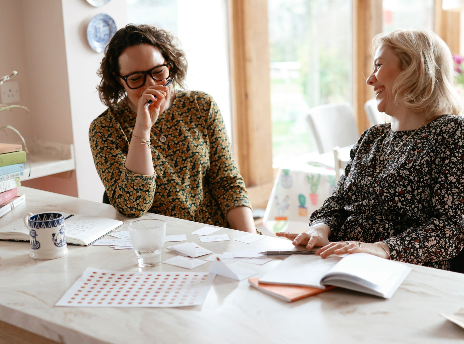 Founders Helly and Rosie, sat at a marble top laughing during a product planning meeting for in this together cards. 